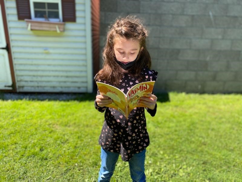young girl reading book outside